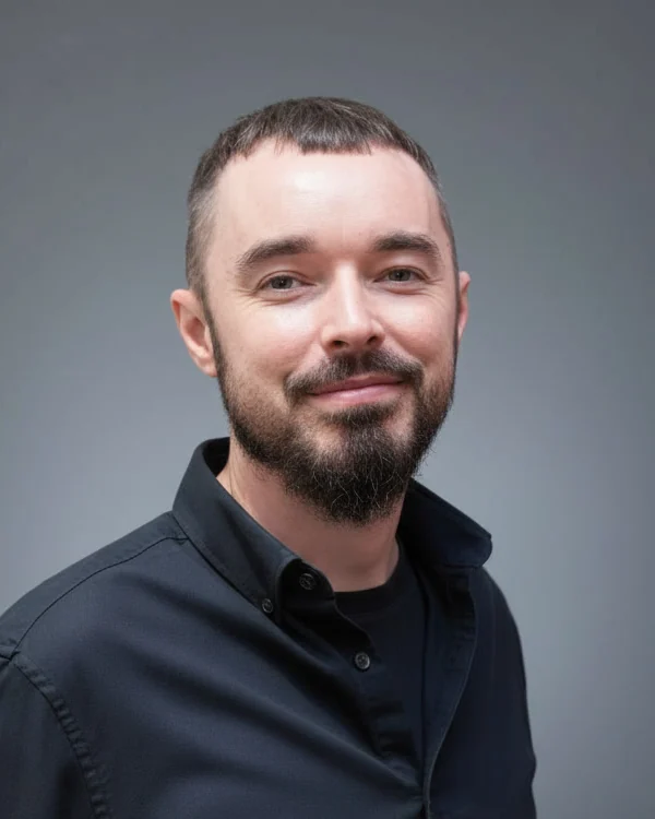 Odhrán Roche smiling, wearing a dark shirt, against a plain grey background.